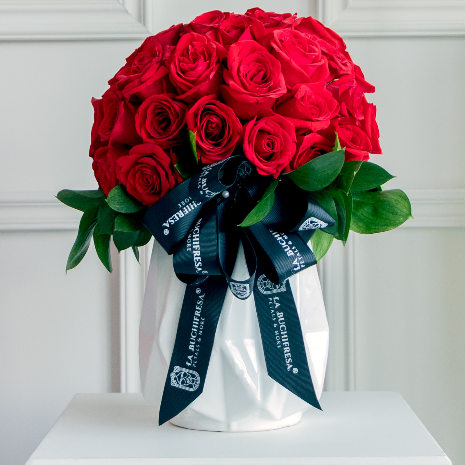 Arreglo en forma de sphera de 50 rosas rojas premium sobre base de ceramica blanca con un moño de liston negro