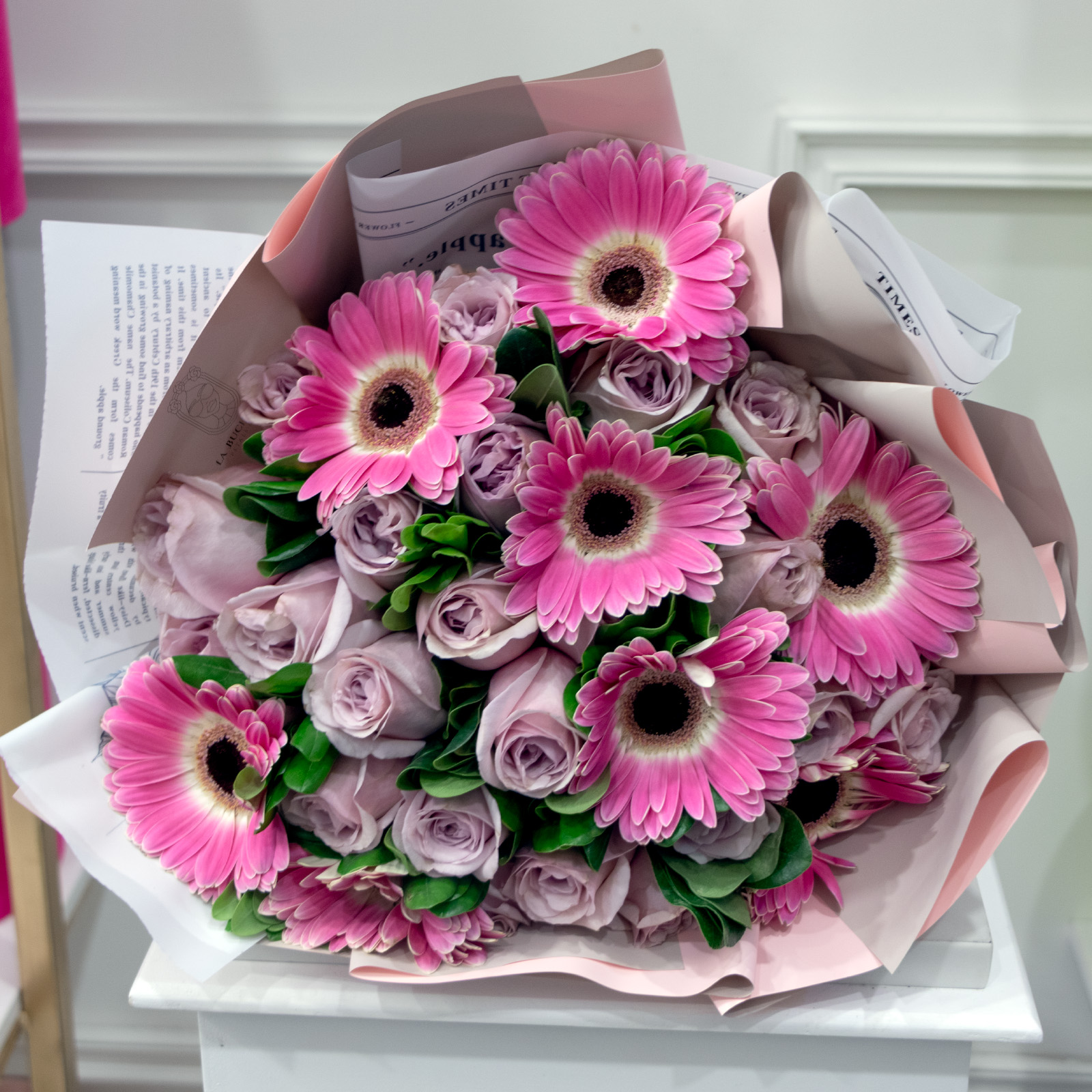 Ramo de 25 rosas lila premium con 8 gerberas rositas con toques de clavo envuelto en papel coreano y liston