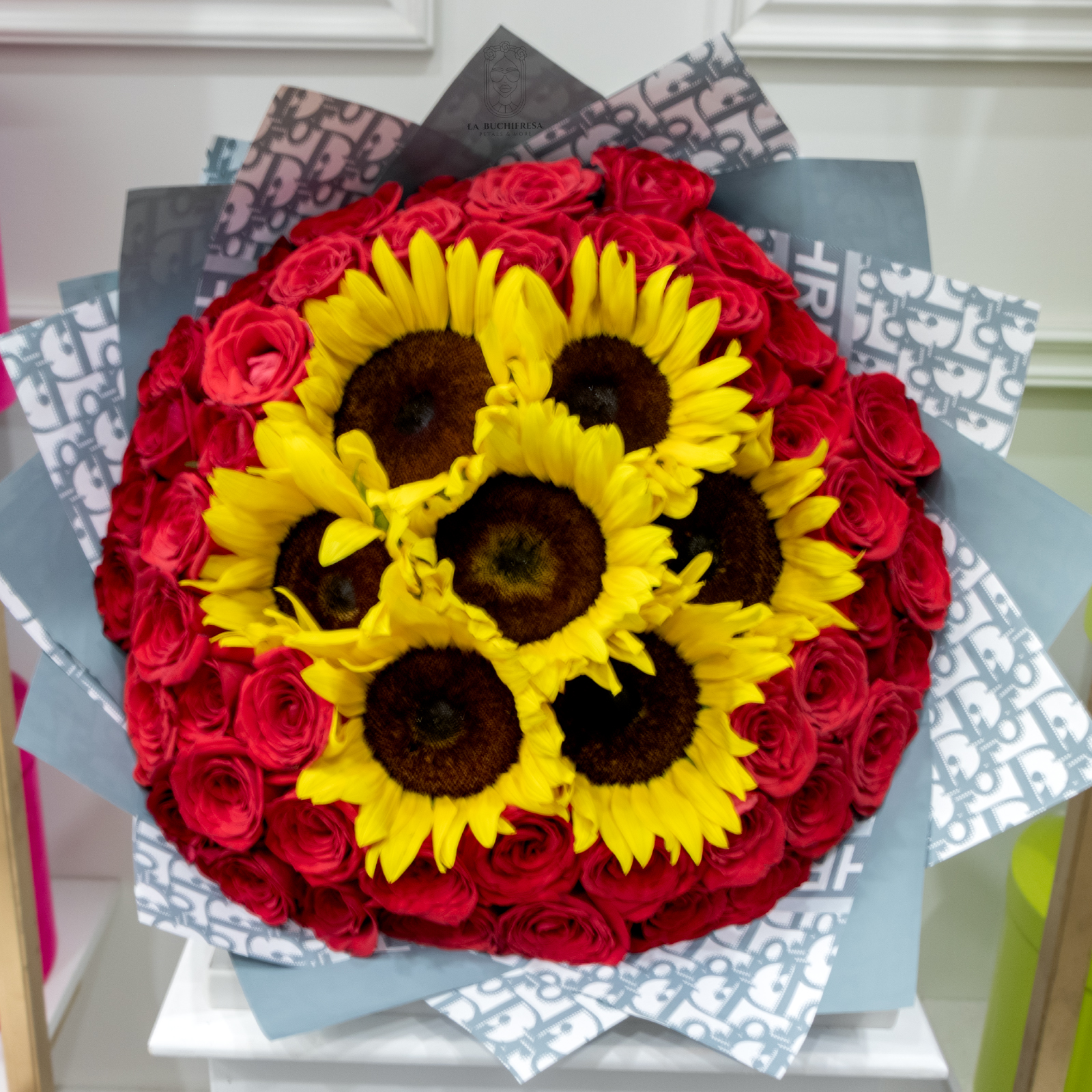 Ramo de 50 rosas rojas premium con 7 girasoles en el centro envuelto en papel coreano y liston