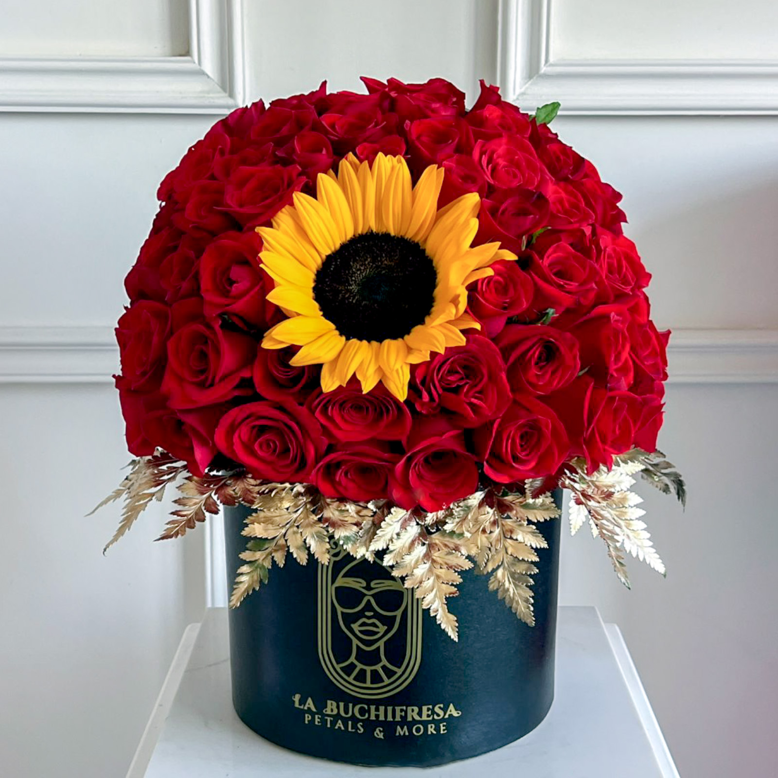 Arreglo de 75 rosas rojas premium en forma de media esfera con un girasol en medio y dolar pintado de dorado alrededor sobre base de madera negra circular