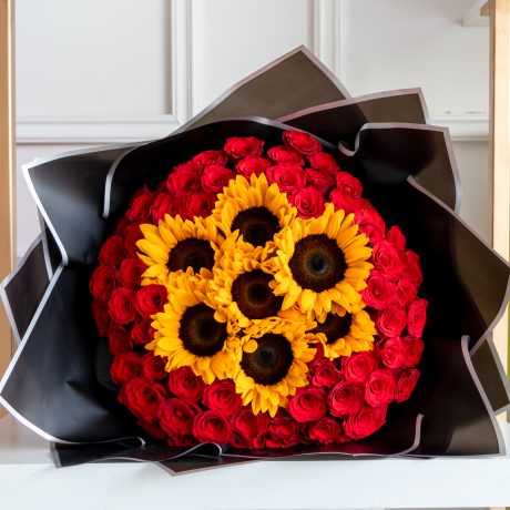 Ramo de 75 rosas rojas premium con 7 girasoles en el centro envuelto en papel coreano y liston